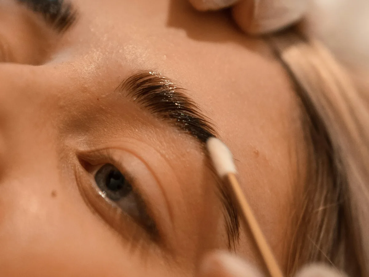 Brow lamination solution being applied to a brushed up eyebrow