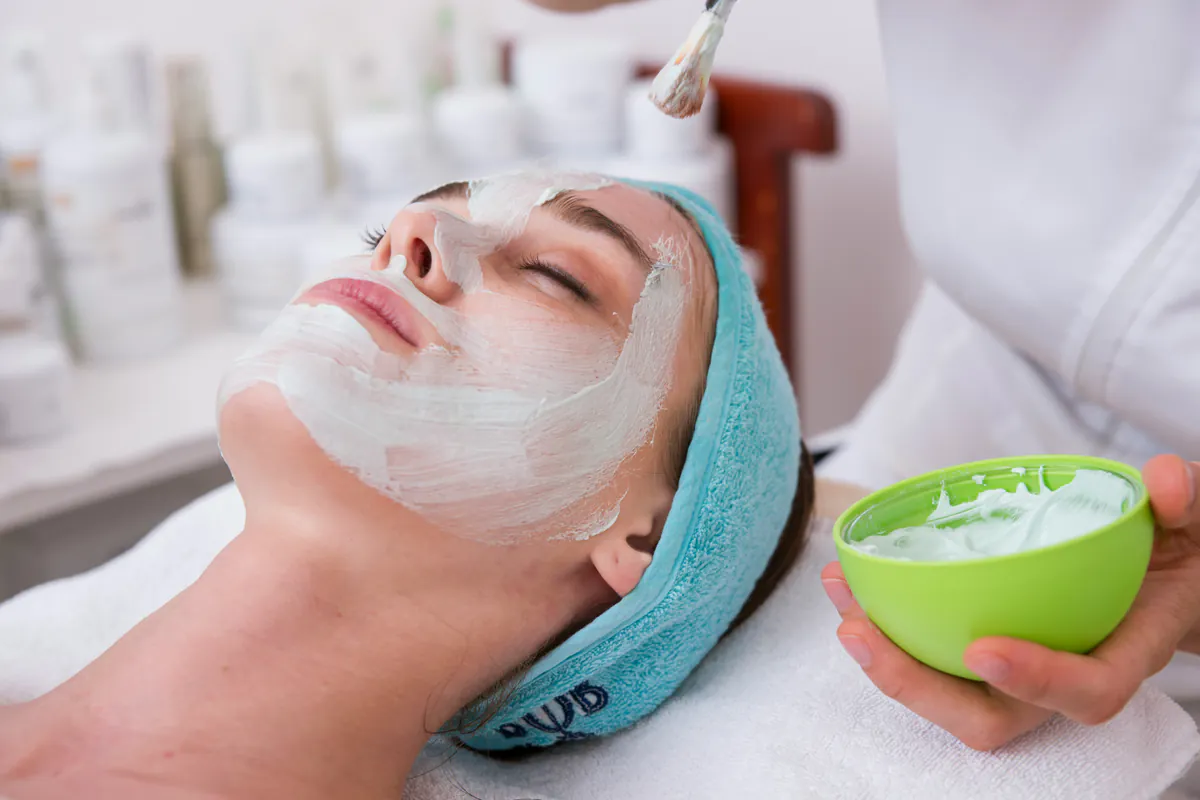 An esthetician brushing peel solution onto a client's face